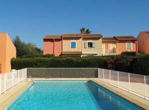 Una piscina con valla blanca, rodeada de casas con techos de tejas rojas y paredes color crema.