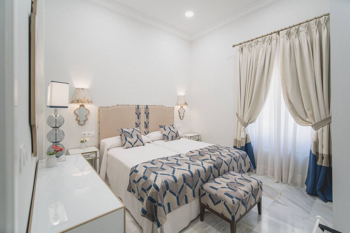 A hotel room with a large bed, bedside tables, a desk, and a window with curtains.
