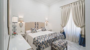 A hotel room with a large bed, bedside tables, a desk, and a window with curtains.
