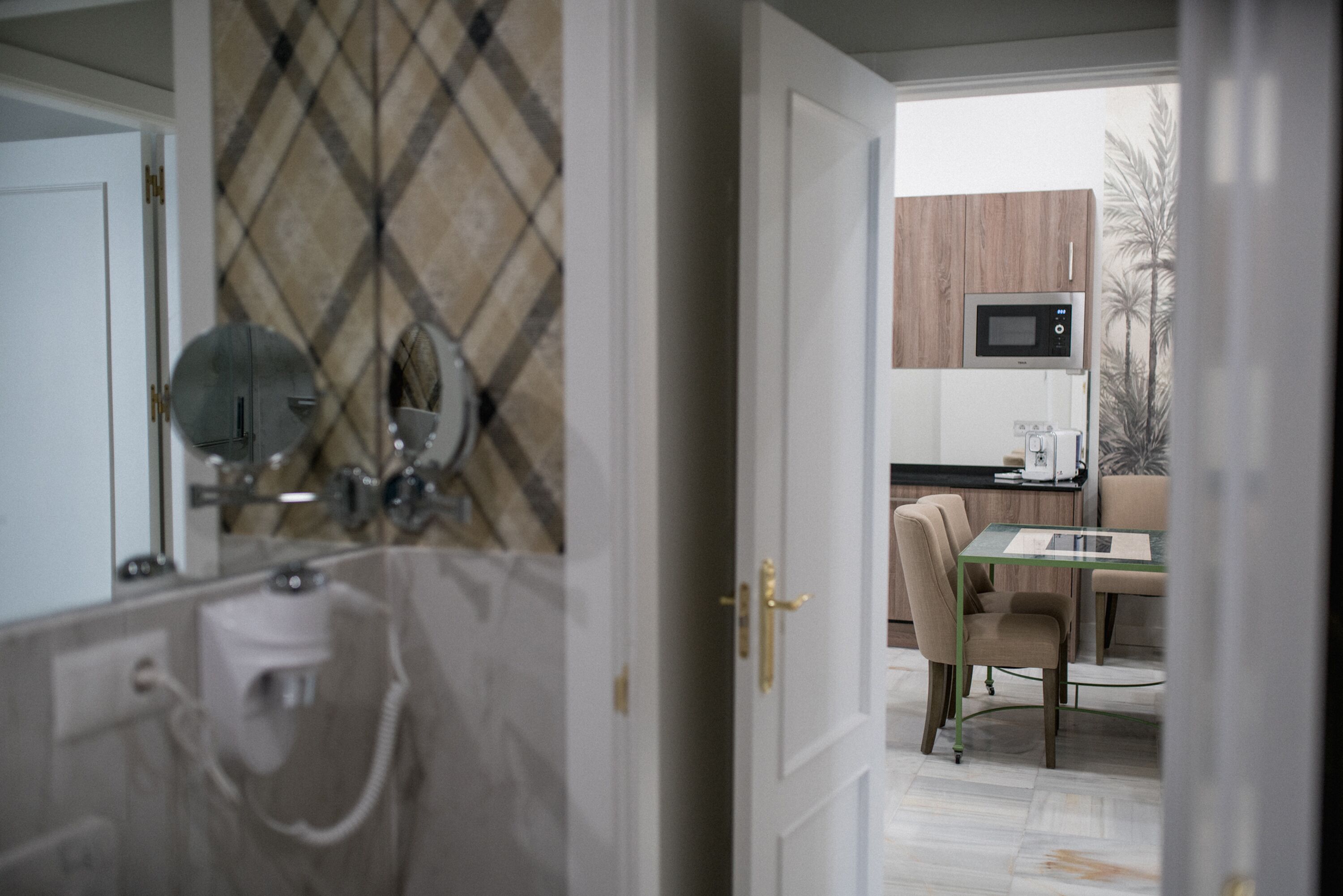 A modern bathroom with a shower, a toilet, and a sink. There is a glass door leading to a dining area with a table and chairs.