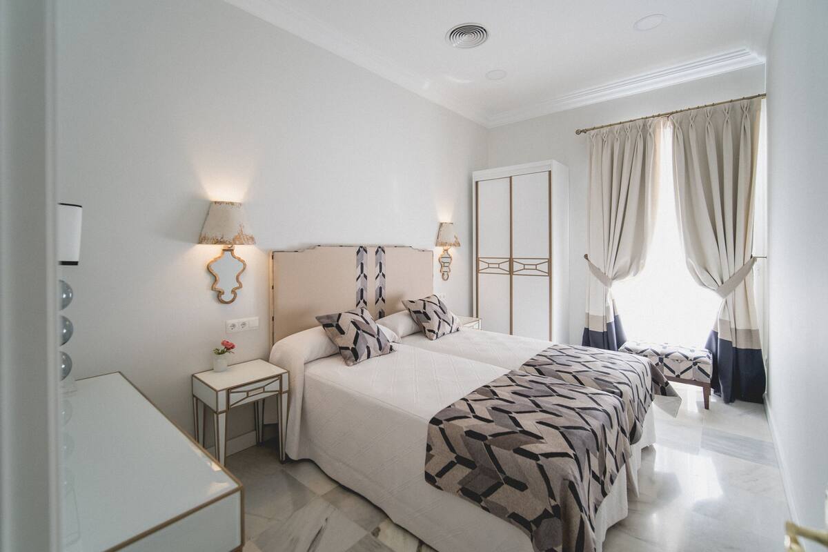 A hotel room with a large bed, bedside tables, a mirror, and curtains.