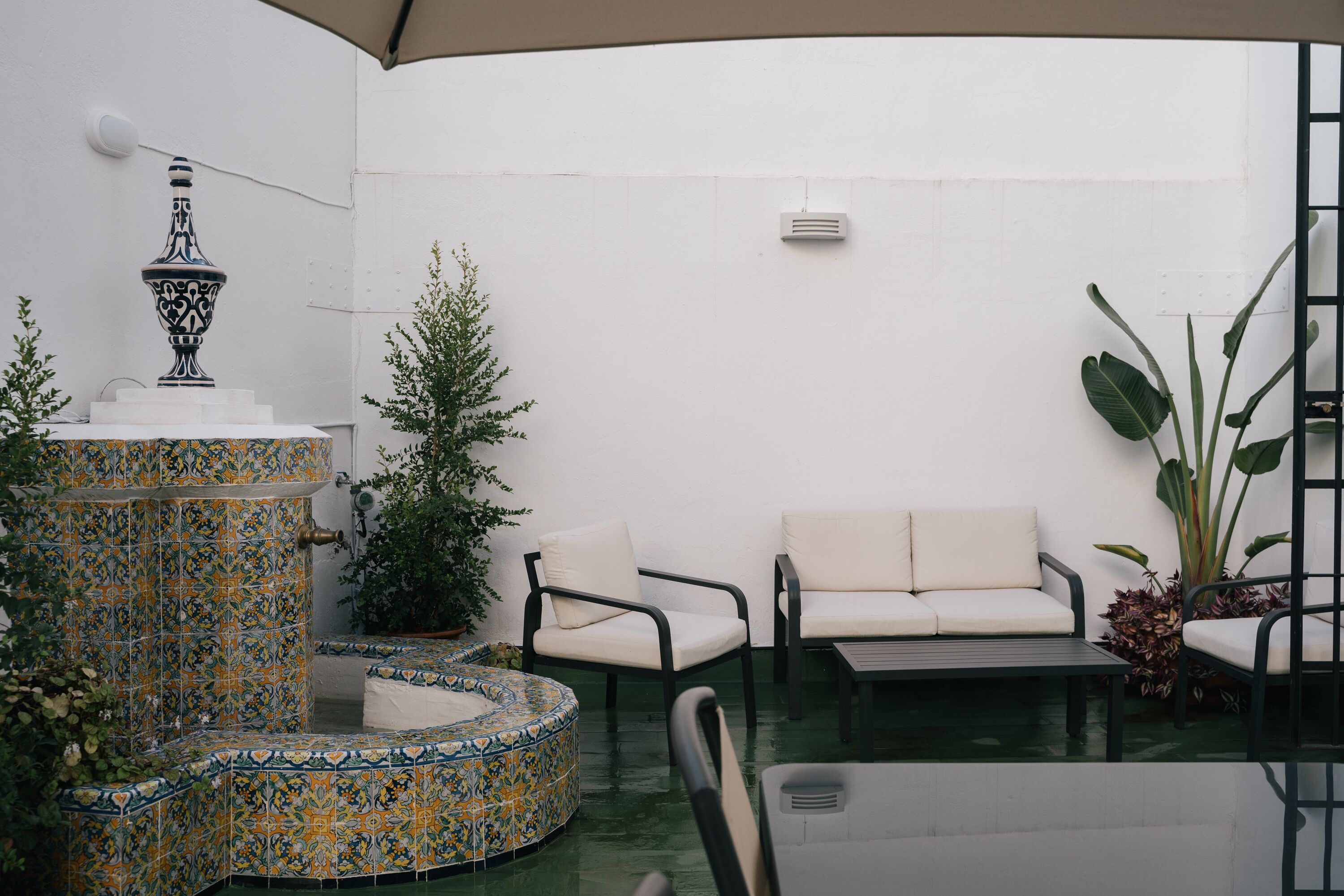 Un patio con una fuente de azulejos, asientos al aire libre y macetas con plantas.