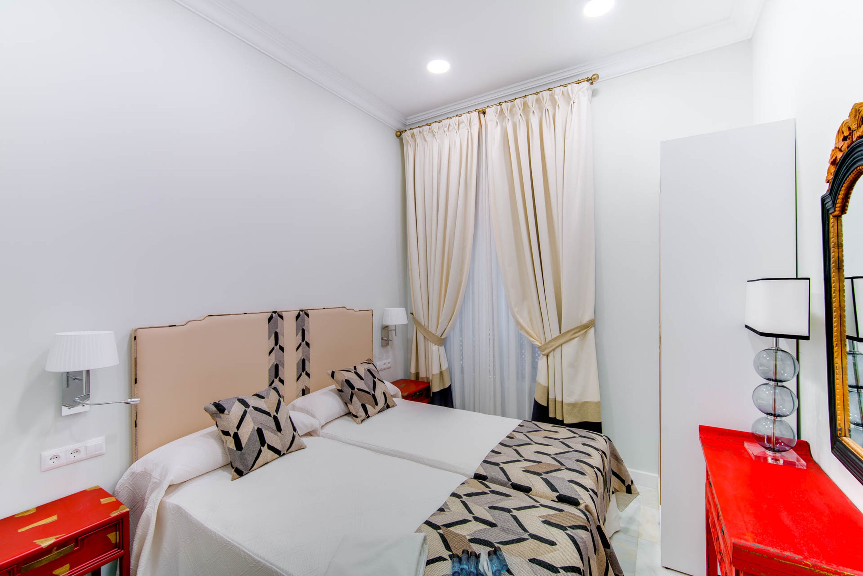 Ein Hotelzimmer mit Bett, Nachttischen, einem Spiegel und einer roten Kommode.