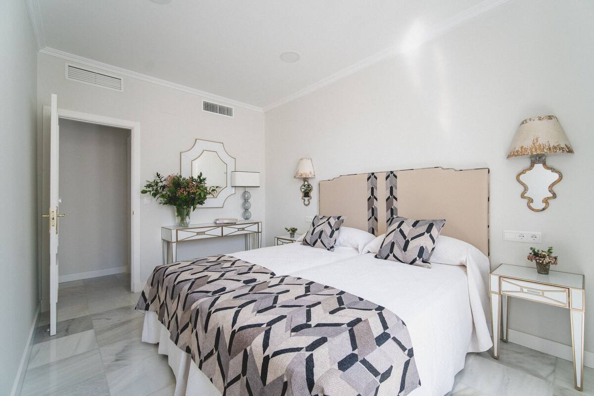 A bedroom with a bed, bedside tables, a desk, and a lamp.