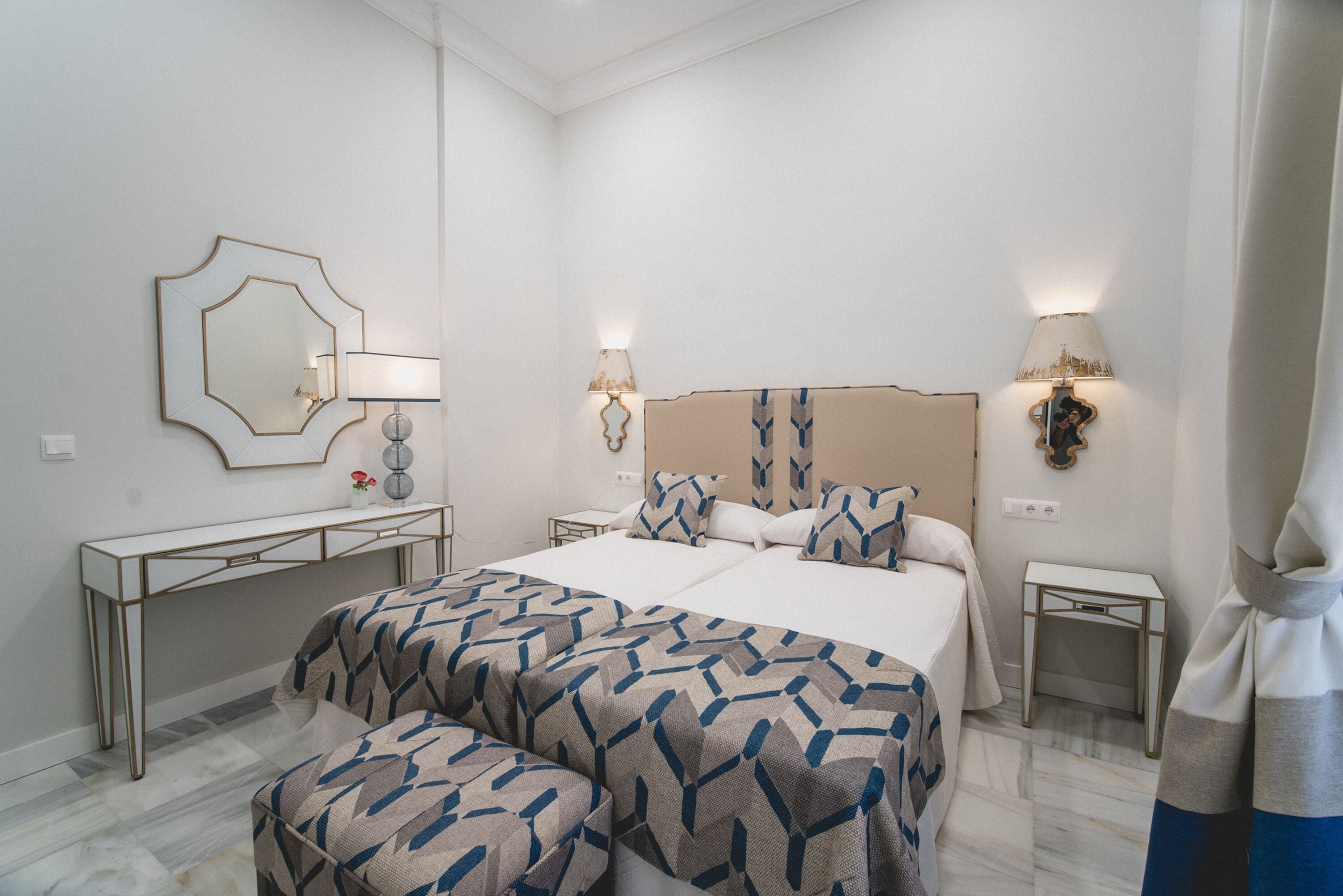 Une chambre d’hôtel moderne avec un grand lit, deux tables de chevet, une console et un grand miroir.