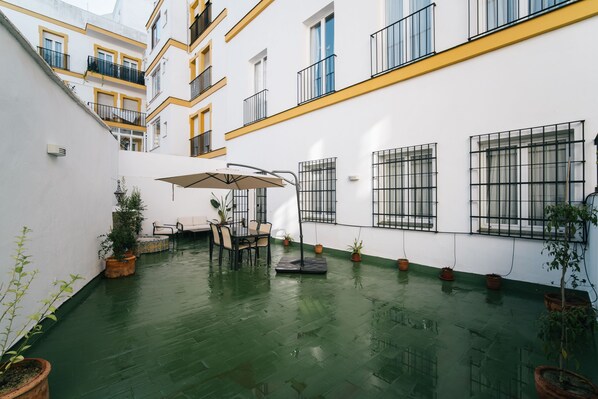 Un patio con una mesa y sillas, plantas en macetas y piso verde.