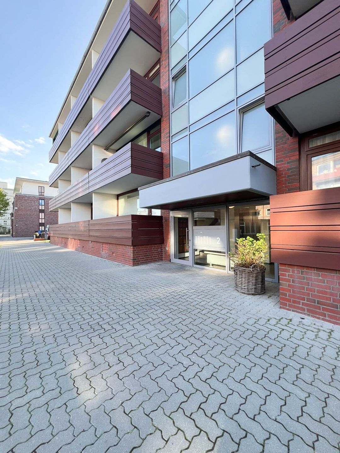 Un bâtiment moderne avec une façade en briques, de grandes fenêtres et un espace d’entrée pavé.