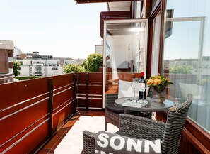 Een balkon met een ronde tafel, rieten stoelen, een fles wijn en een vaas met bloemen.