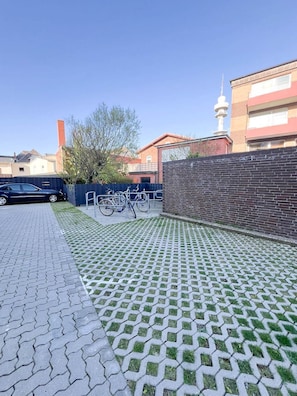 Un chemin piétonnier dallé, orné d’un motif décoratif, un mur en briques et un vélo appuyé contre ce mur.