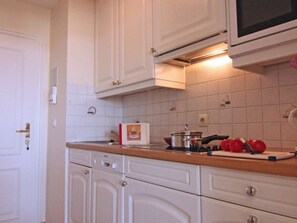 A kitchen with white cabinets, a microwave, and a countertop with a pot, tomatoes, and a cutting board.