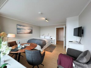 A hotel room with a bed, a desk with a chair, a TV mounted on the wall, and a painting on the wall.