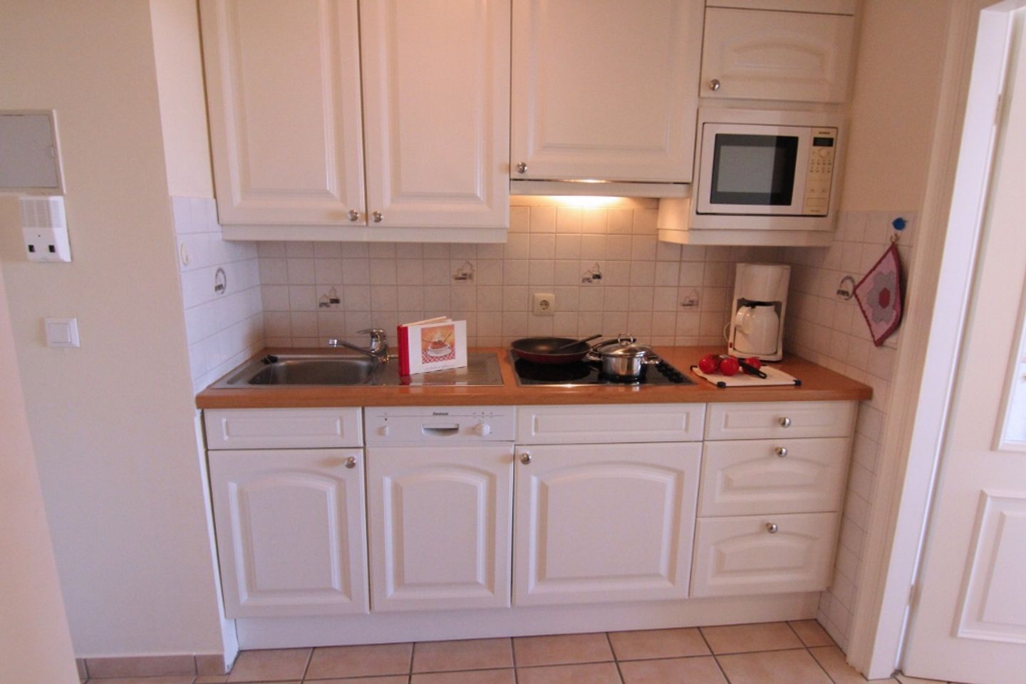 Una cocina compacta con armarios blancos, un microondas, un fregadero y una estufa.