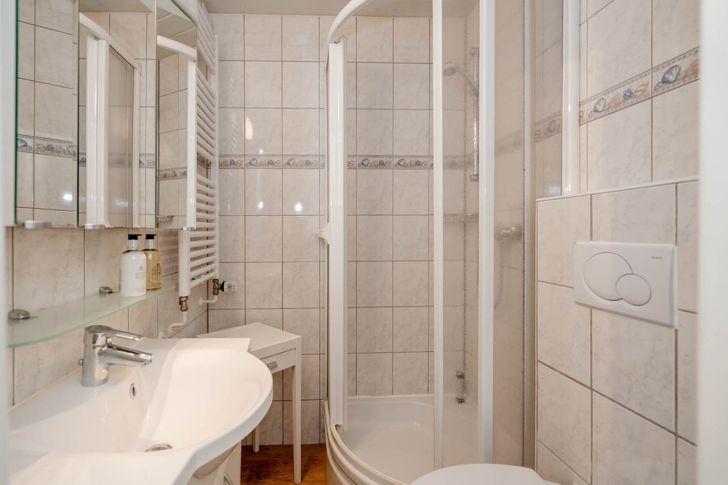 Un baño moderno con cabina de ducha de vidrio, un lavabo blanco y un inodoro.