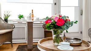 Habitació amb una cadira de vímet, una taula de fusta amb una bandeja, un ram de flors i una ampolla de xampany.