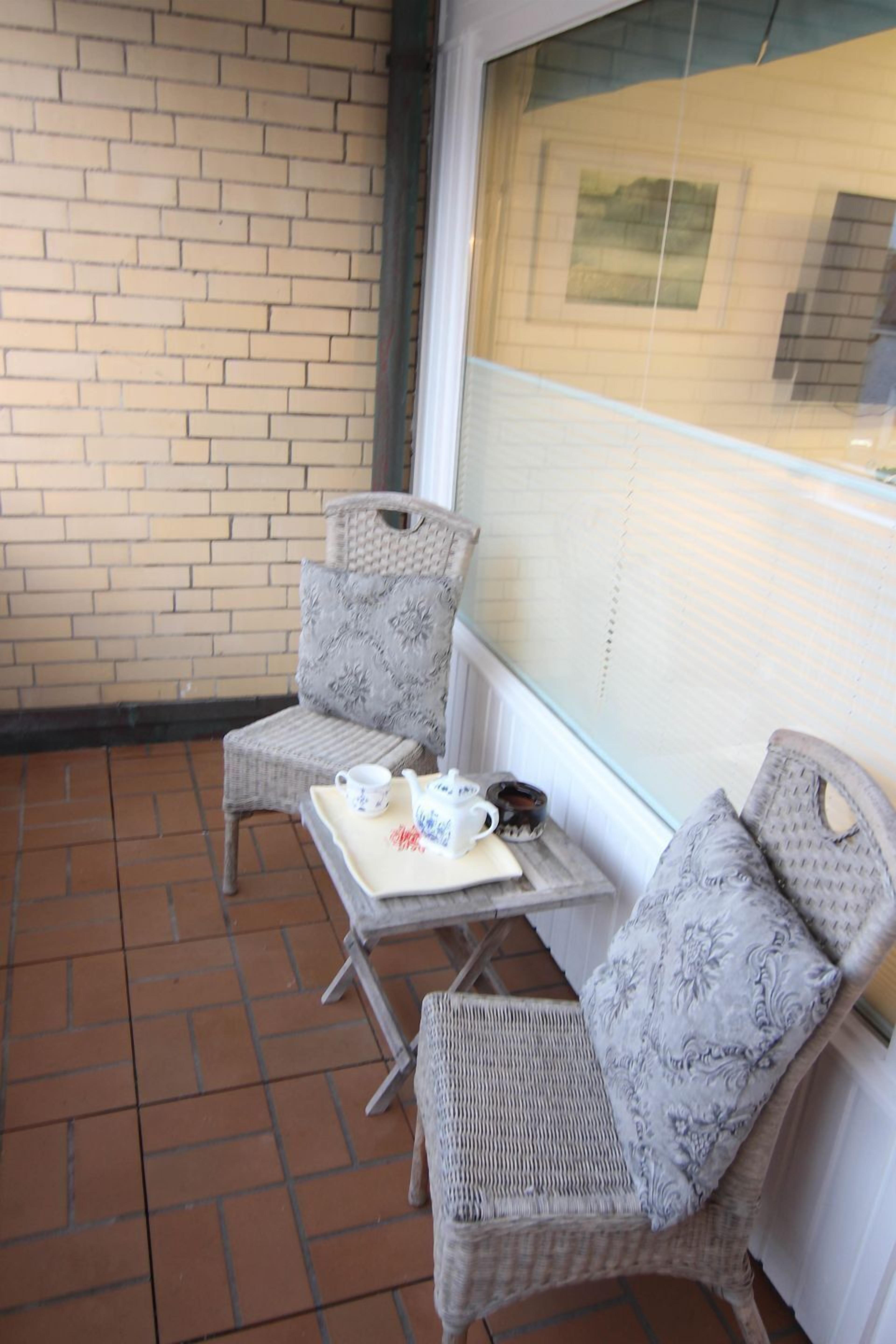 Ein kleiner Außenbereich mit Korbstühlen und einem Tisch, mit einer Ziegelwand und einem Fenster mit Jalousien.