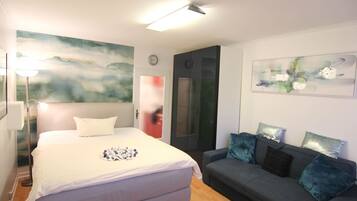 Ein Schlafzimmer mit einem Bett, einem grauen Sofa mit Kissen, einem Bild an der Wand und einer Tür mit Milchglasfenster.