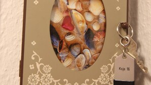 A wall-mounted clock with a seashell design and a key attached. - Koje16 - Very cozy, adorably small and yet perfectly equipped. (Sylt)