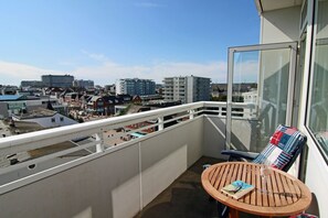 Un balcón con vistas a la ciudad, una mesa con un libro y un vaso, y una silla con cojín a rayas.