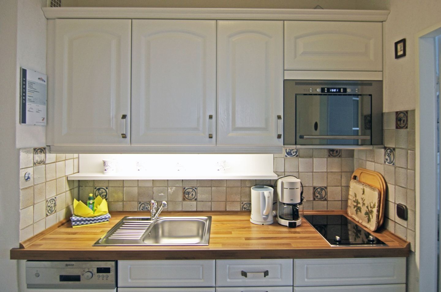 A kitchen with white cabinets, a stainless steel sink, a microwave, and a coffee maker.