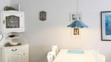 Ein Essbereich mit weißem Tisch und Stühlen, einer weißen Kommode mit Glastür, einer blauen Pendelleuchte und gerahmten Bildern an der Wand.