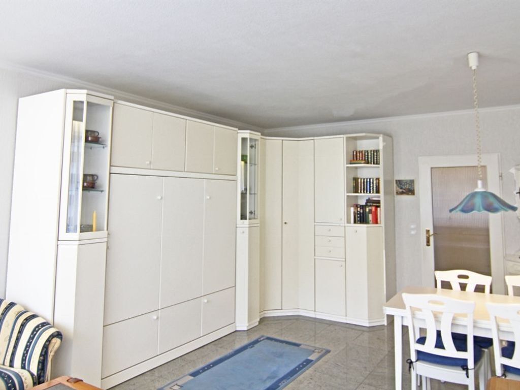 A room with a dining table, chairs, a blue rug, and white cabinets with shelves.
