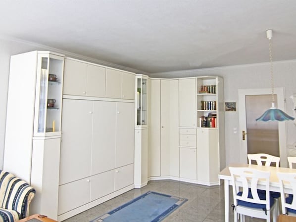A room with a dining table, chairs, a blue rug, and white cabinets with shelves.