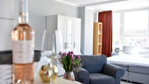 Una habitación de hotel moderna con un sofá gris, una cama, un ventanal con cortinas y un minibar.