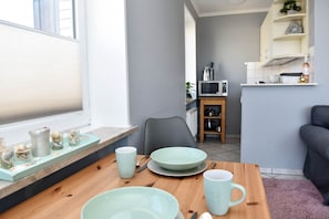 Un comedor con una mesa de madera, platos verde claro y tazas. Una silla está colocada junto a la mesa.