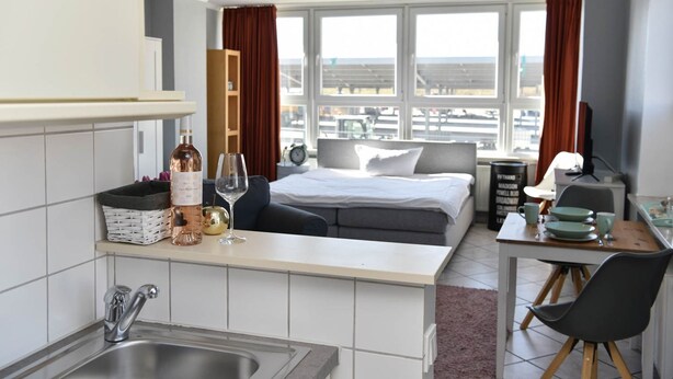 Una habitación de hotel compacta con kitchenette, una cama, zona de comedor y un amplio ventanal con vistas a la ciudad.
