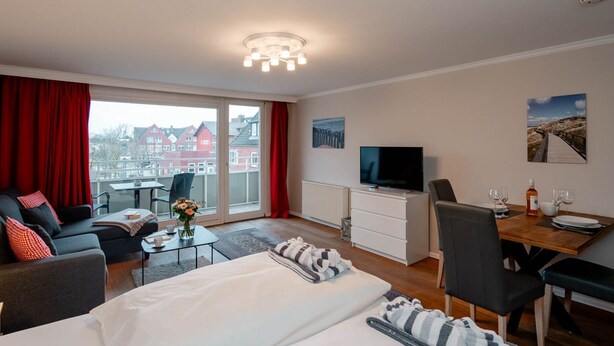 Une chambre d’hôtel moderne avec un grand lit, un bureau, une télévision et un balcon agrémenté de rideaux rouges.