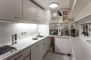 Een kleine keuken met witte kastjes, een magnetron, een koffiezetapparaat en diverse keukengerei dat aan de muur hangt.
