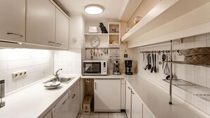 Une cuisine compacte avec des meubles blancs, un four à micro-ondes encastré, une machine à café et des ustensiles de cuisine accrochés au mur.