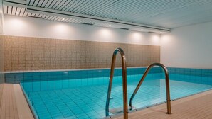 Une piscine intérieure avec des carreaux bleu clair, un sol carrelé et un escalier métallique.