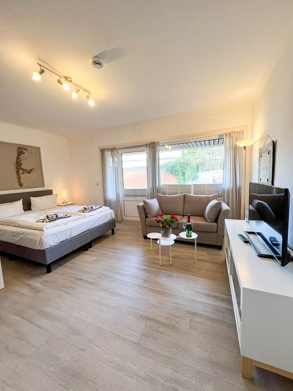 A hotel room with a bed, sofa, TV, and a small table with a vase of flowers.