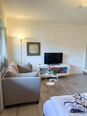 A modern living room with a sofa, a flat-screen TV, a small coffee table with a vase of flowers, and a wall-mounted picture.