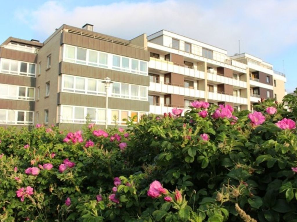 Un edificio residencial de varios pisos con balcones y un jardín con flores rosadas.