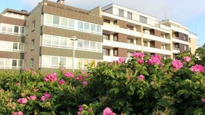 Ein mehrstöckiges Wohnhaus mit Balkonen und einem Gartenbereich mit rosa Blumen.