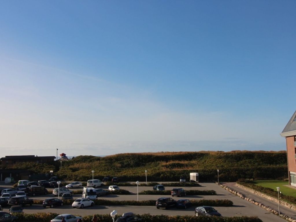 A parking lot with multiple cars, a building with a sloped roof, and a grassy hill in the background.