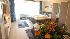 Ein modernes Hotelzimmer mit Bett, Schreibtisch, Stuhl, einem kleinen Balkon und einem großen Fenster.