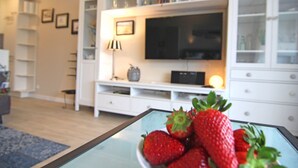 Ein modernes Wohnzimmer mit einem Glastisch, der Erdbeeren hält, einem Flachbildfernseher auf einer weißen Unterhaltungsanlage und einer Lampe.
