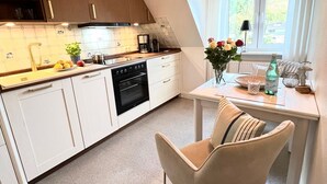 Una cocina moderna con armarios blancos, horno integrado y comedor con mesa y sillas.