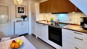 Una cocina moderna con armarios blancos, encimera de madera y horno empotrado. Hay una mesa de comedor con un frutero y un florero.