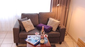 Ein modernes Wohnzimmer mit grauem Sofa, zwei Zierkissen, einer violetten Decke, einem kleinen Tisch mit Buch, einem Glas Wein und einer Kerze.