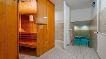 Ein Saunaraum mit Holzwänden und einer Glastür, der zu einem gefliesten Badezimmer mit einem blauen Duschbereich führt.