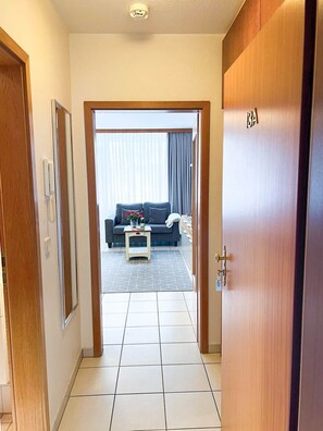 Un pasillo que conduce a una sala de estar con un sofá, una mesita de centro y una puerta con la leyenda 'BA'.