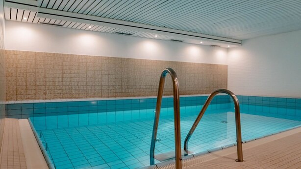 Ein Hallenbad mit hellblauen Fliesen, einem gefliesten Boden und einer Metallleiter.