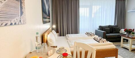 A hotel room with a dining table set for breakfast, a sofa, and a bed.