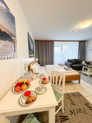 A hotel room with a dining table set for breakfast, a sofa, and a bed.
