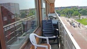 A balcony with a view of a street and buildings. There are two chairs and a table on the balcony. - Strönwai - Perfect for sunbathing or enjoying the vacation life of the Strandstraße (Sylt)