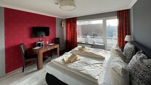 A hotel room with a bed, a desk with a computer, a TV, and a window with curtains. - Strönwai - Perfect for sunbathing or enjoying the vacation life of the Strandstraße (Sylt)